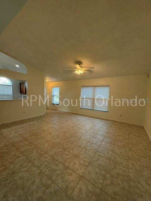 An empty living room features beige tile flooring, a ceiling fan, and large windows — 1930 TEABERRY COURT, ORLANDO, FL