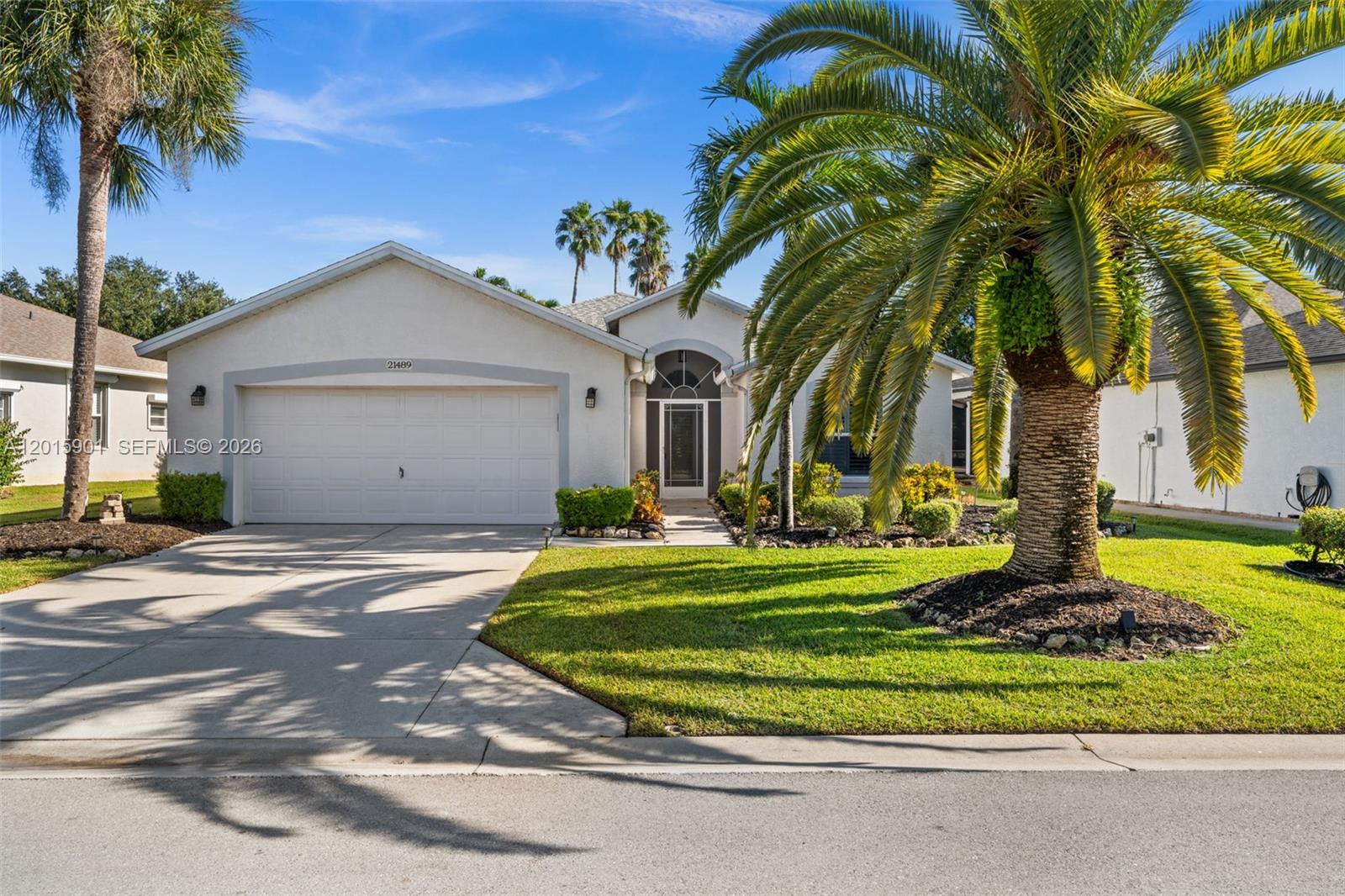 A single-story house with a white stucco exterior, a two-car garage, and a large palm tree — 21489 SHERIDAN RUN, Estero FL 33928, ESTERO, FL