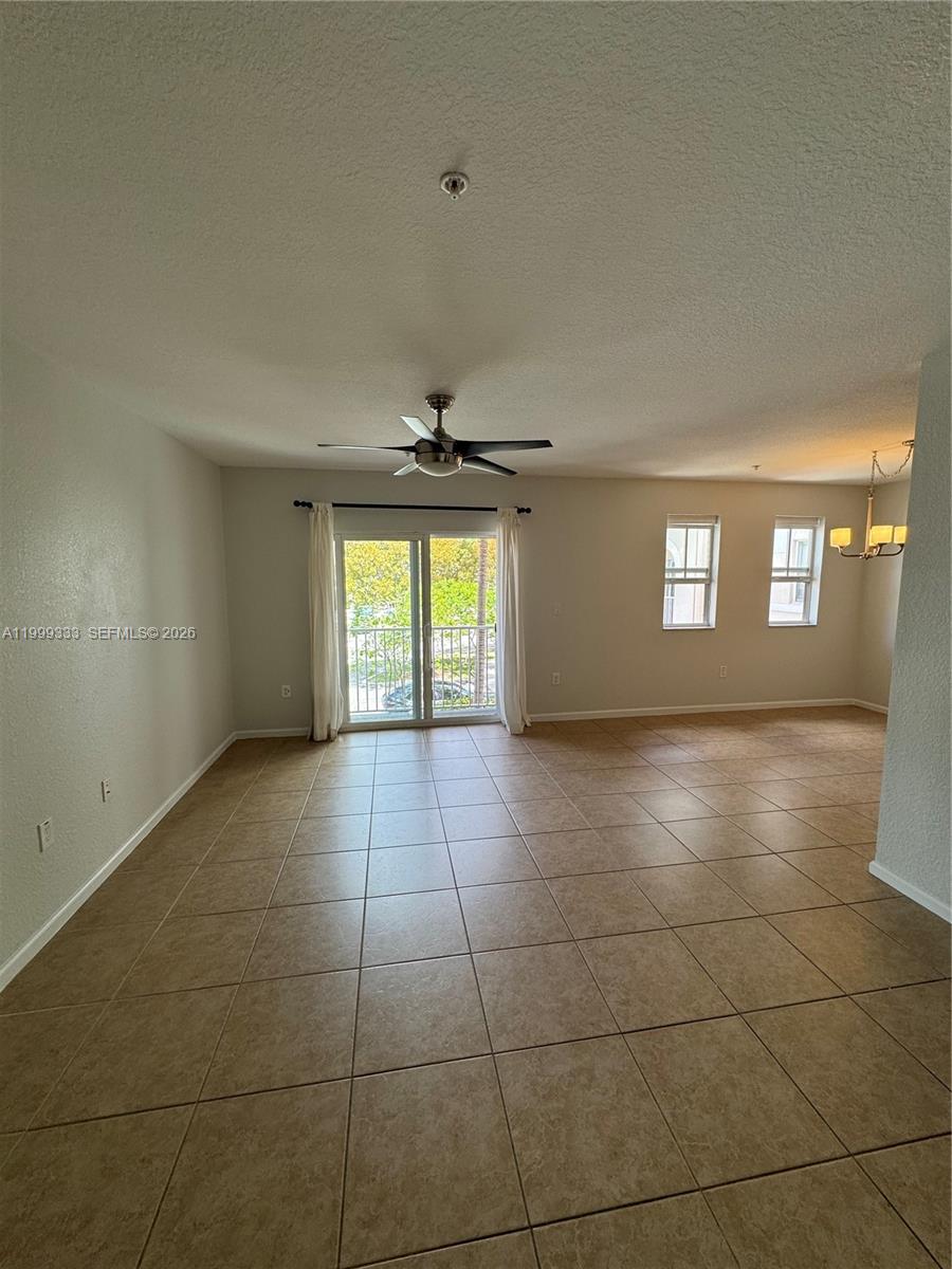 An empty living room features beige tile flooring, a ceiling fan, and a sliding glass door — 11601 NW 89th St # 209, Doral FL 33178, DORAL, FL