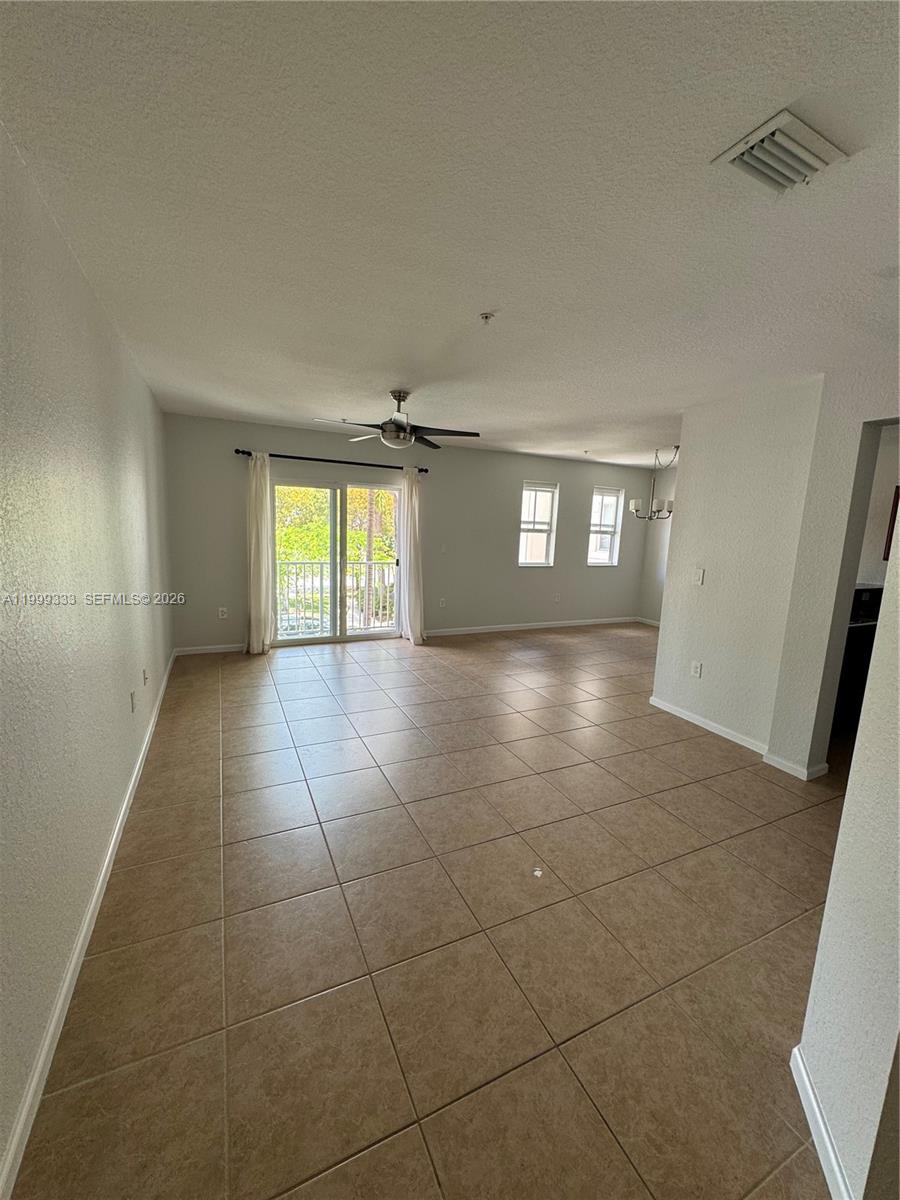 An open-concept living and dining area features beige tile flooring, a ceiling fan, and sliding glass doors — 11601 NW 89th St # 209, Doral FL 33178, DORAL, FL