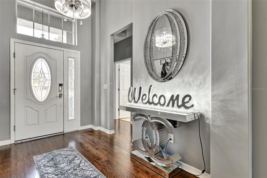 A foyer features dark hardwood floors, a white front door, and a mirrored console table — 7514 FOREST MERE DRIVE, RIVERVIEW, FL