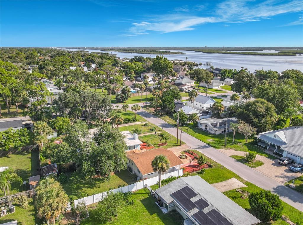 An aerial view shows a residential neighborhood with houses, lush trees, and a nearby waterway — 906 FERNALD STREET, EDGEWATER, FL