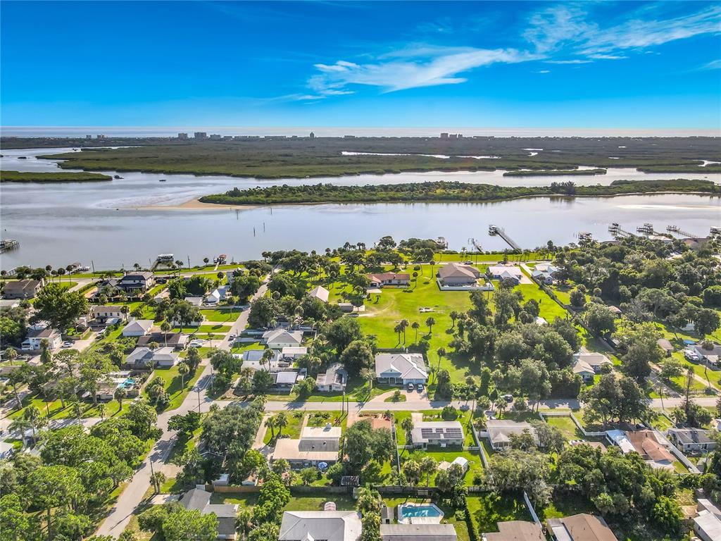 An aerial view shows a residential neighborhood situated along a waterway with distant coastal buildings — 906 FERNALD STREET, EDGEWATER, FL