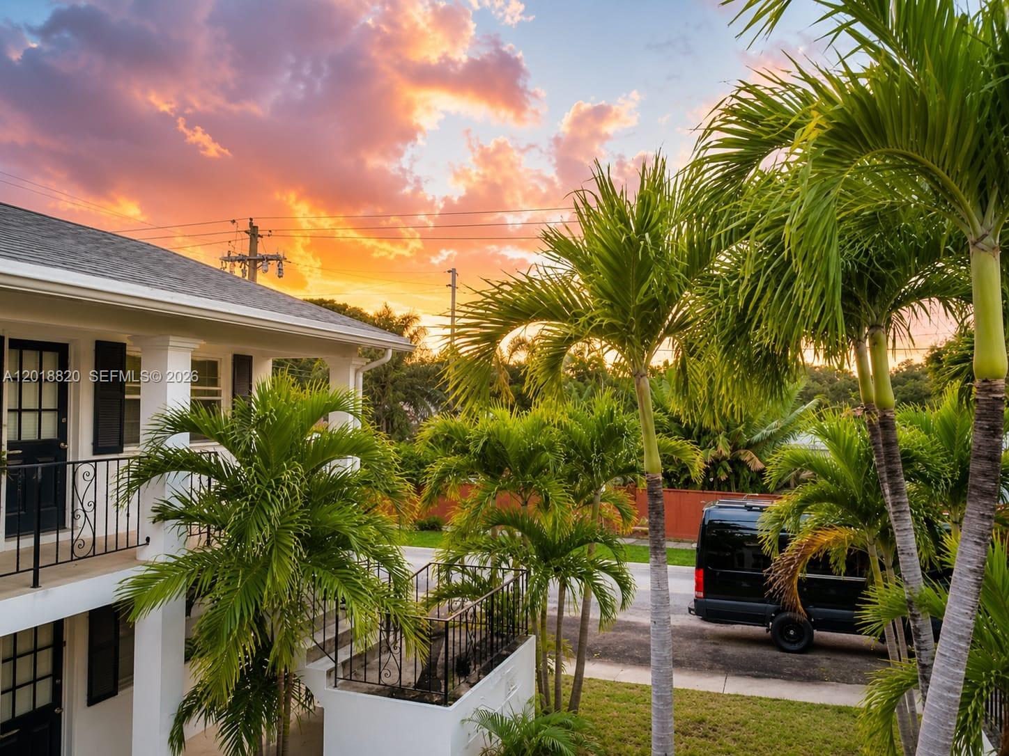 A two-story white building with a black door and palm trees under a sunset sky — HOLLYWOOD, FL