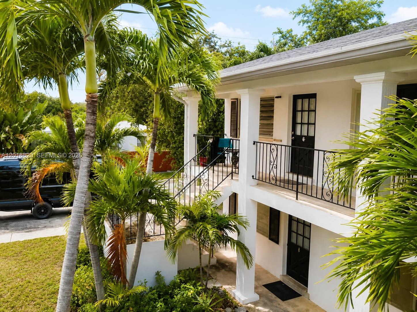 A two-story white building features a black metal staircase and balcony railings with palm trees — HOLLYWOOD, FL