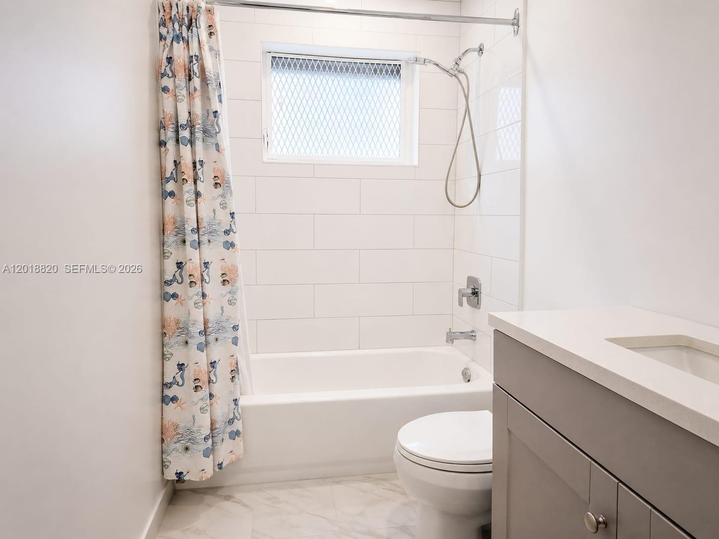 A bathroom features a white tiled shower-tub combination, a gray vanity, and a toilet — HOLLYWOOD, FL