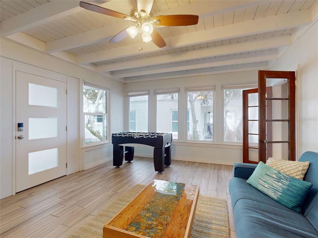 A sunroom features a foosball table, a blue sofa, a wood-topped coffee table, and white-painted beams — 1011 Hill STREET, NEW SMYRNA BEACH, FL