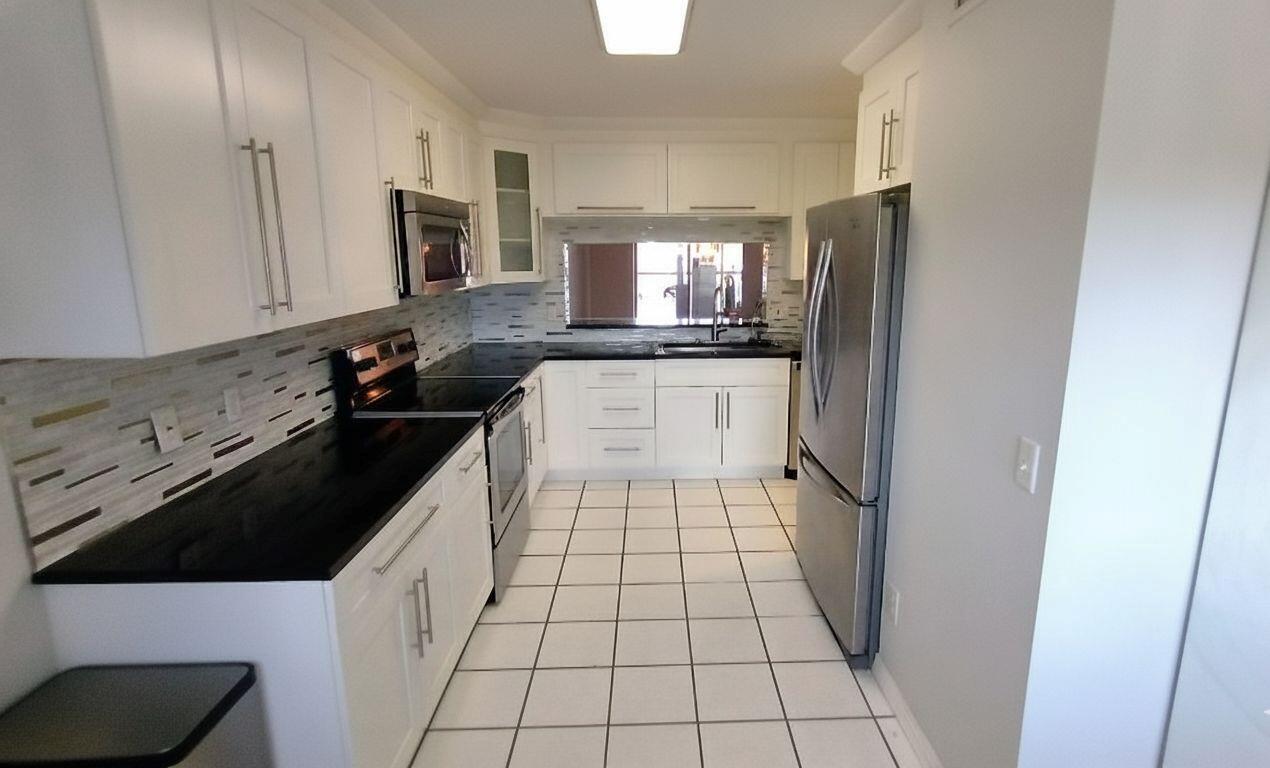 A galley kitchen features white cabinets, black countertops, stainless steel appliances, and white tile flooring — 4735 E Lucerne Lakes Boulevard E # 413, Lake Worth FL 33467, LAKE WORTH, FL