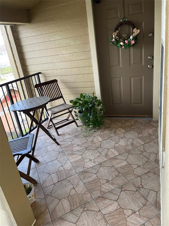 A balcony features a small wooden table, two folding chairs, a potted plant, and tiled flooring — 2210 GRAND CAYMAN COURT UNIT 1737, KISSIMMEE, FL