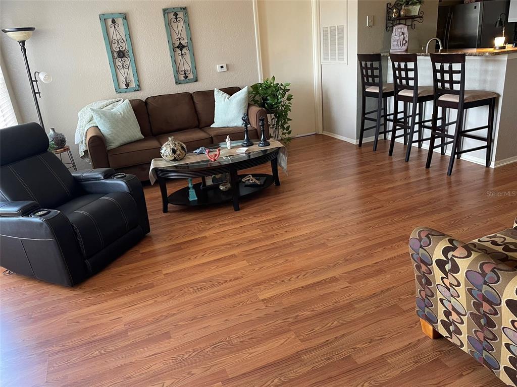 A living room features wood-look flooring, a brown sofa, a black recliner, and bar seating — 2210 GRAND CAYMAN COURT UNIT 1737, KISSIMMEE, FL