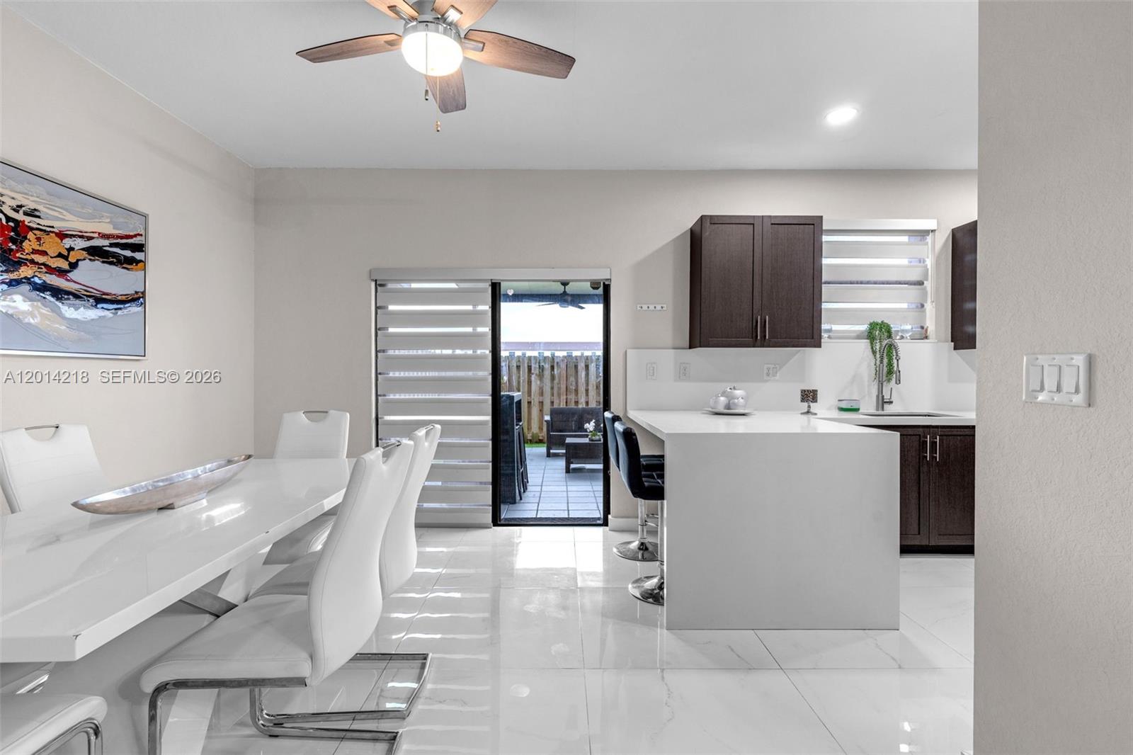 A modern dining area and kitchen feature white tile floors, dark cabinetry, and a patio — 23082 SW 127th Pl # 0, Miami FL 33170, MIAMI, FL