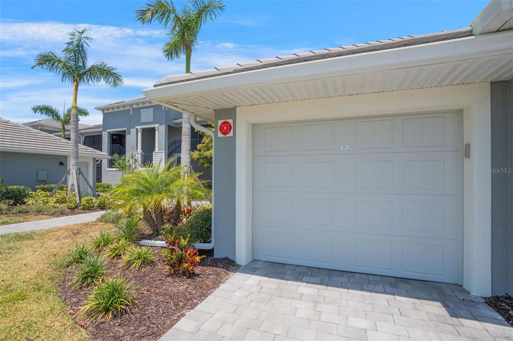 A view of a residential garage exterior with a paved driveway and palm trees — 12440 WELLEN GOLF STREET UNIT 105, VENICE, FL