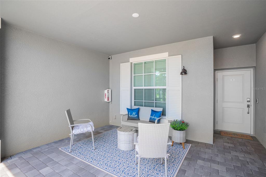 A covered patio features gray paver flooring, a seating area with a rug, and a door — 12440 WELLEN GOLF STREET UNIT 105, VENICE, FL
