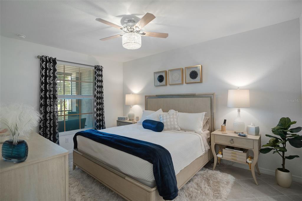 A bedroom features a bed with a blue throw, two nightstands, and a ceiling fan — 12440 WELLEN GOLF STREET UNIT 105, VENICE, FL