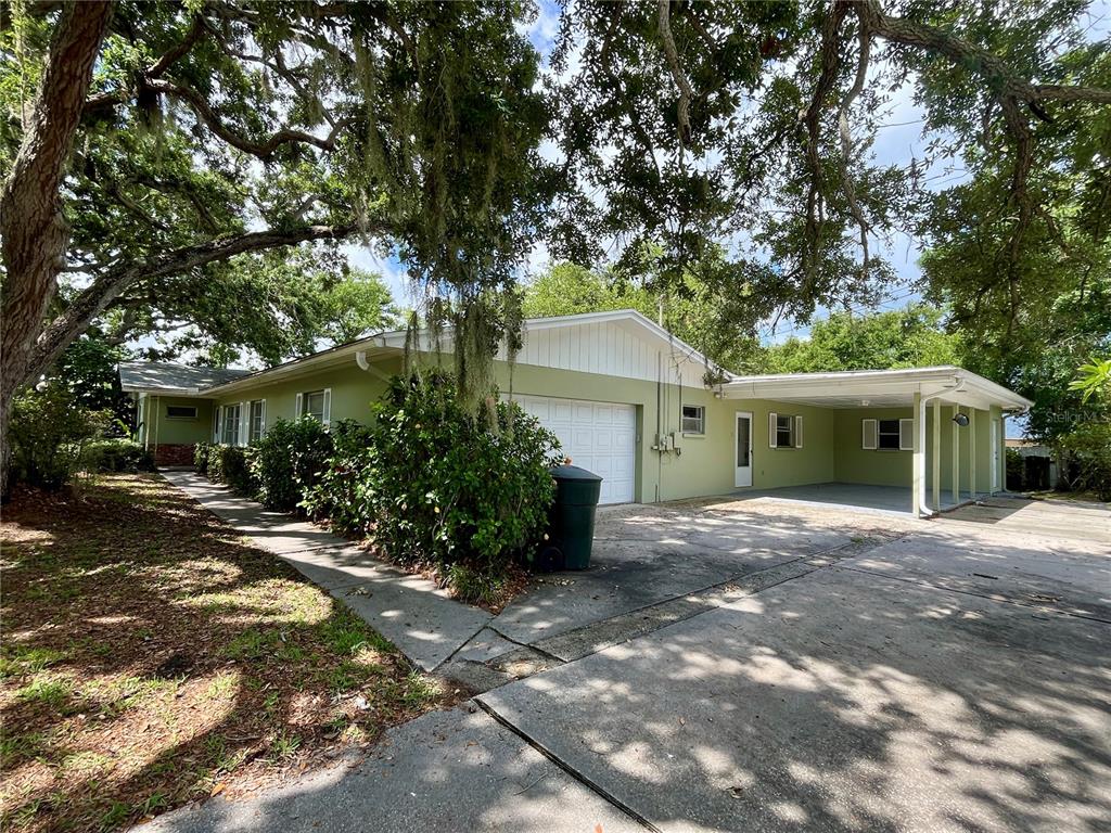 A light green single-story house features a garage, a carport, and mature oak trees — 58 ARNONI DRIVE, DUNEDIN, FL