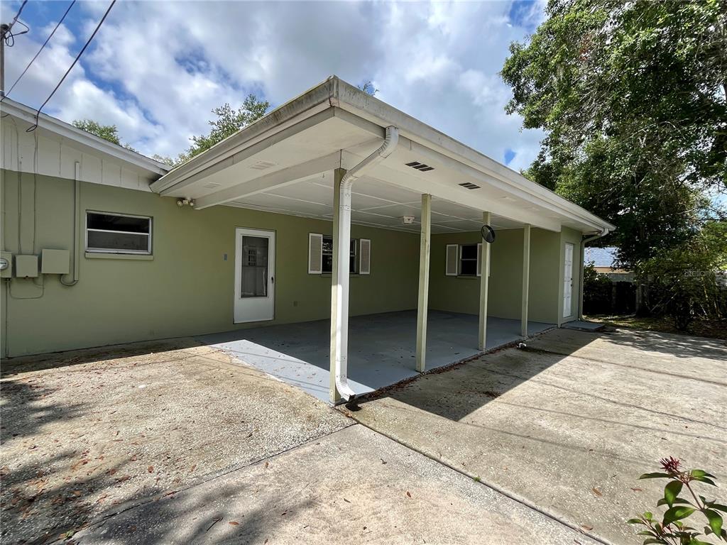 A covered carport with a concrete floor is attached to the side of a house — 58 ARNONI DRIVE, DUNEDIN, FL