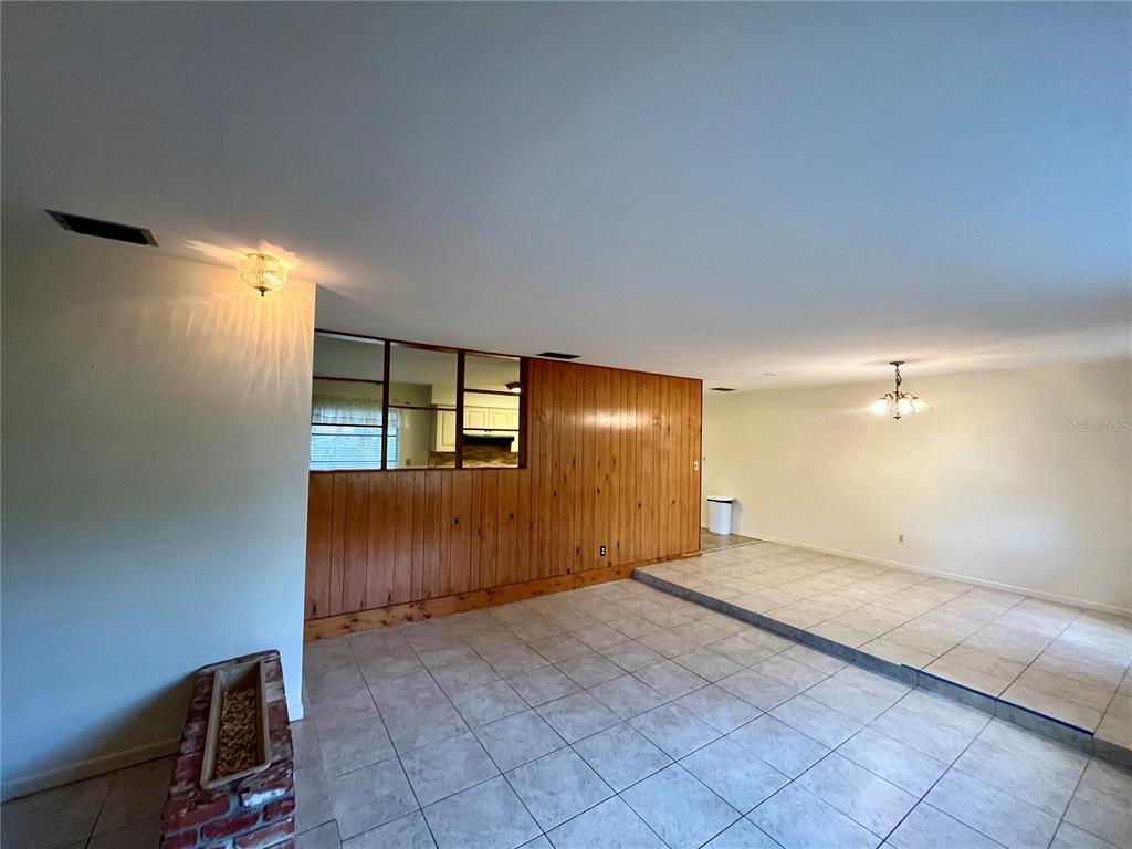 An open-concept living area features wood paneling, tile flooring, and a sunken dining space — 58 ARNONI DRIVE, DUNEDIN, FL