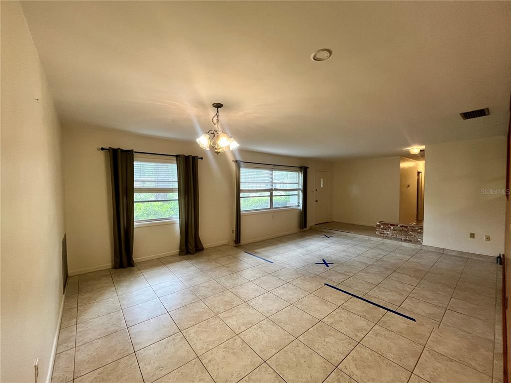A spacious living area features beige tile flooring, two windows with curtains, and a chandelier — 58 ARNONI DRIVE, DUNEDIN, FL
