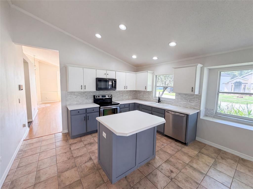 A kitchen features white upper cabinets, gray lower cabinets, a central island, and tile flooring — 701 MAGNOLIA CREEK CIRCLE, ORLANDO, FL