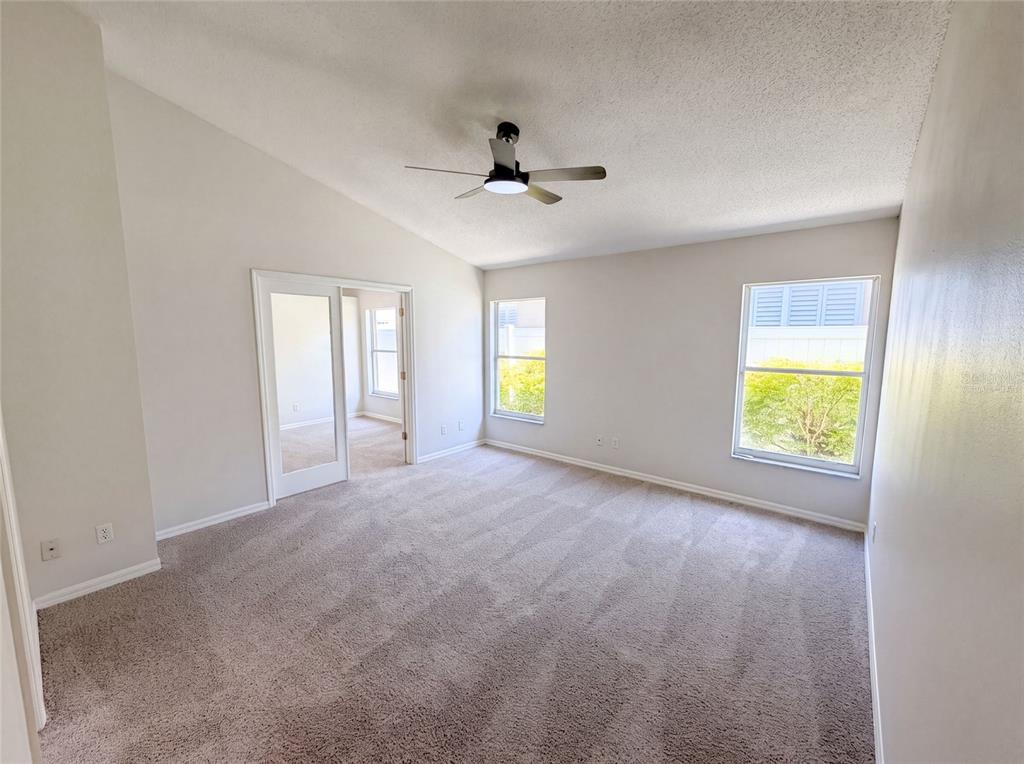 A carpeted bedroom with a vaulted ceiling, a ceiling fan, and glass-paned double doors — 701 MAGNOLIA CREEK CIRCLE, ORLANDO, FL