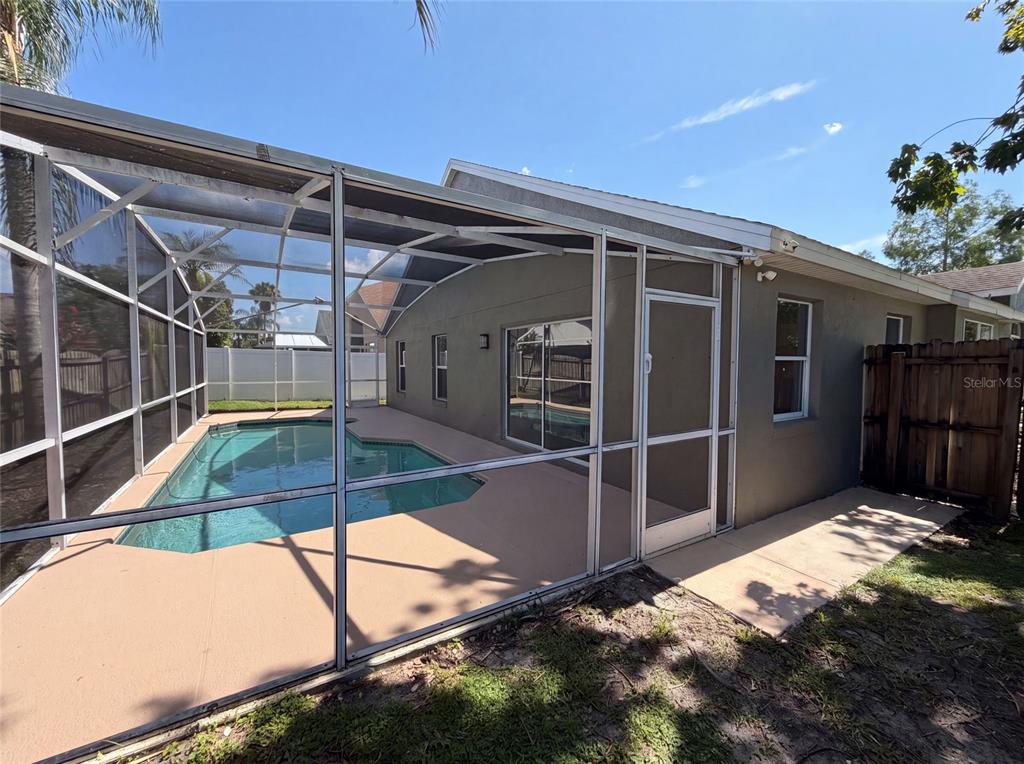A screened-in pool enclosure with a concrete patio sits beside a house with tan siding — 701 MAGNOLIA CREEK CIRCLE, ORLANDO, FL