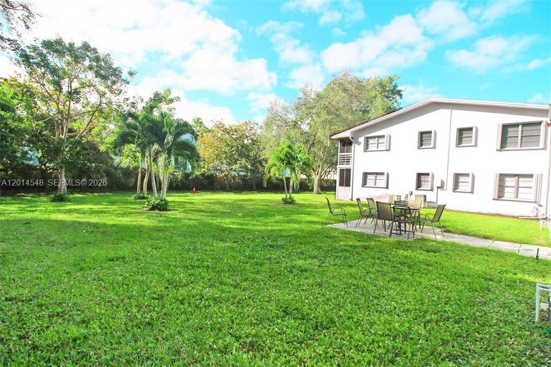 A grassy backyard with palm trees and a patio area beside a multi-story building — 70 Prescott D # 70, Deerfield Beach FL 33442, DEERFIELD BEACH, FL