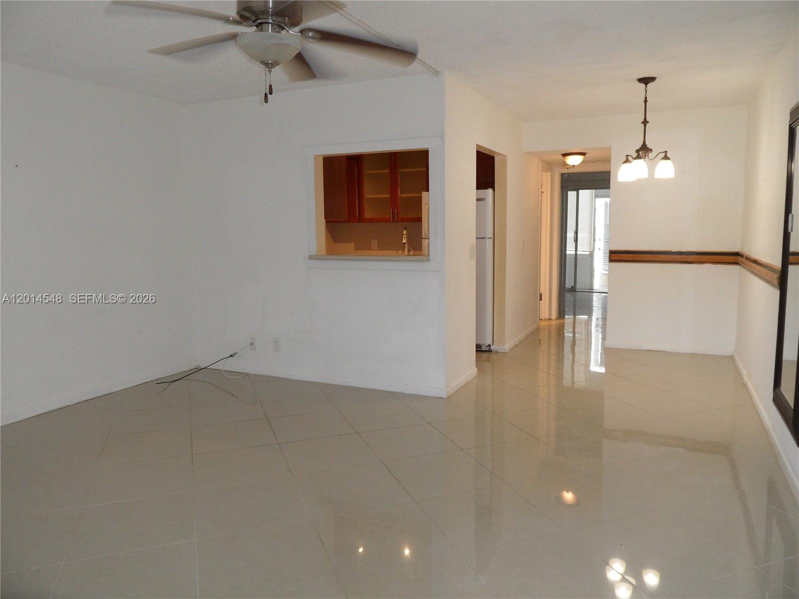 An open-concept living and dining area features white walls, tile flooring, and a kitchen pass-through — 70 Prescott D # 70, Deerfield Beach FL 33442, DEERFIELD BEACH, FL