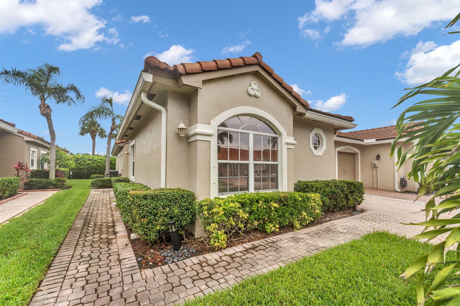 A beige stucco house with a tiled roof, arched window, and brick paver walkway — 8385 Vía Serena, Boca Raton FL 33433, BOCA RATON, FL