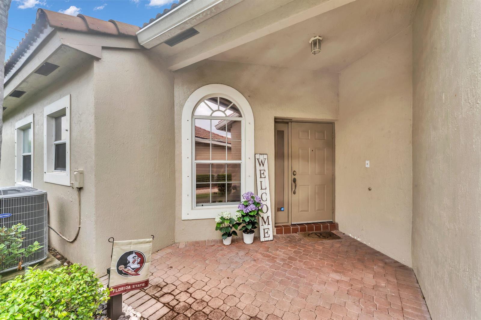 The exterior entrance features a brick-paved porch, a tan front door, and an arched window — 8385 Vía Serena, Boca Raton FL 33433, BOCA RATON, FL