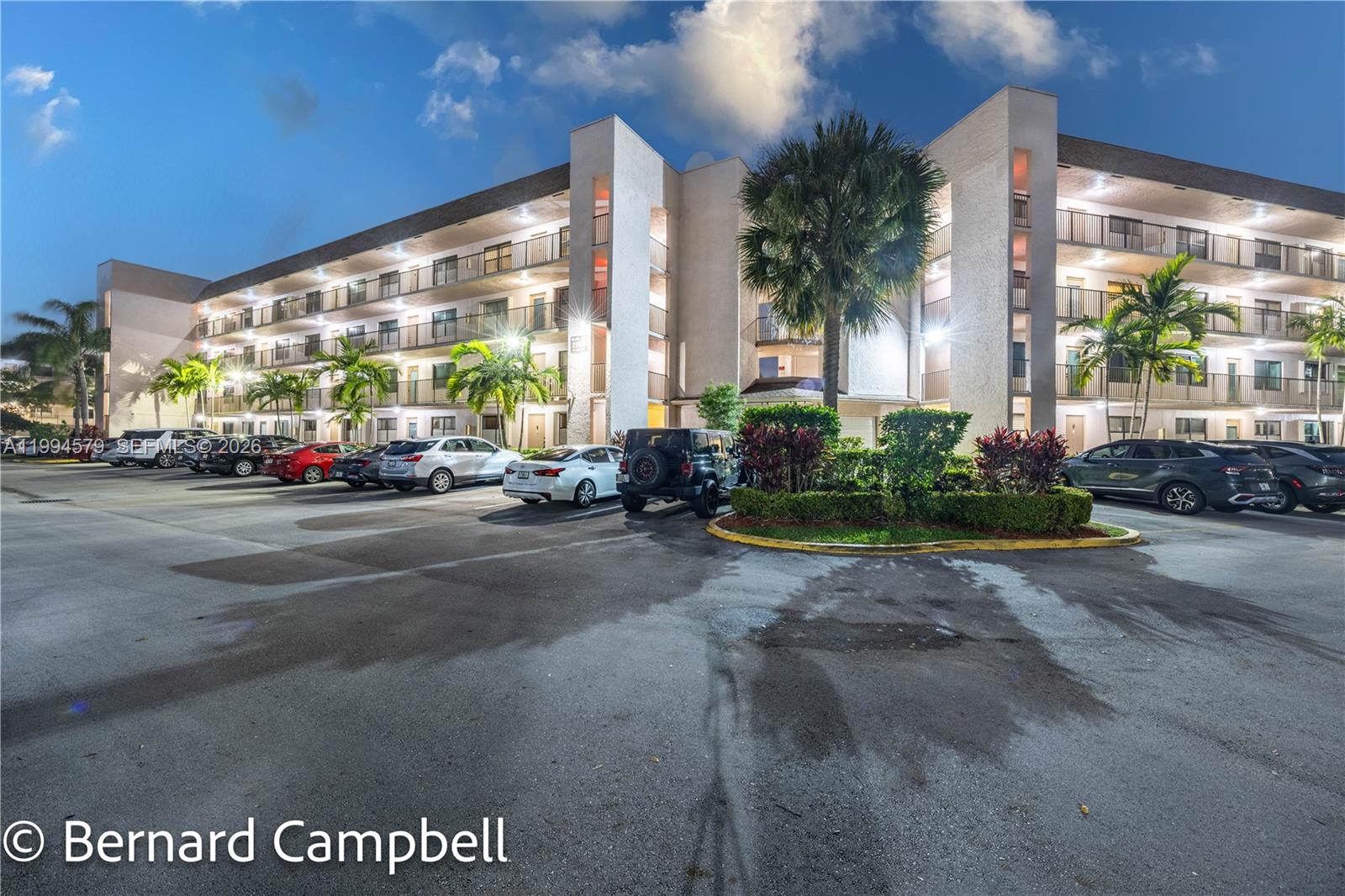 A multi-story apartment building with a parking lot and palm trees at dusk — 2606 NW 104th Ave # 303, Sunrise FL 33322, SUNRISE, FL
