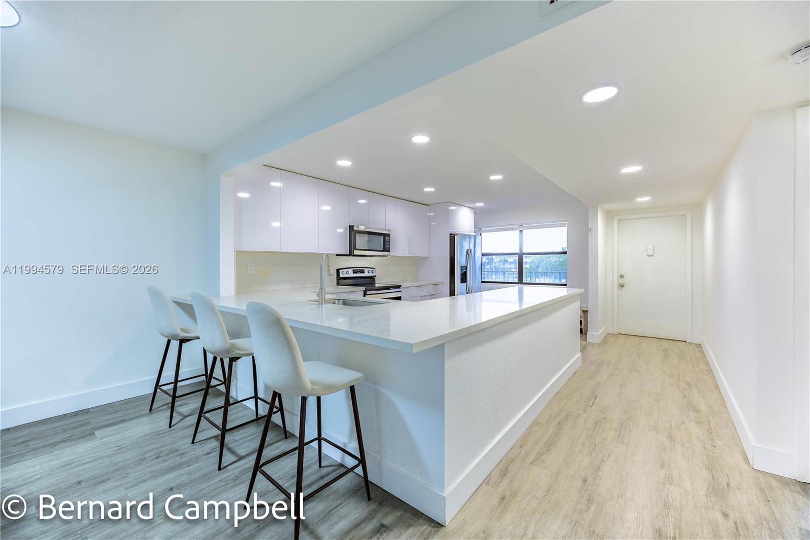 A modern kitchen features white cabinetry, quartz countertops, a breakfast bar, and light wood flooring — 2606 NW 104th Ave # 303, Sunrise FL 33322, SUNRISE, FL