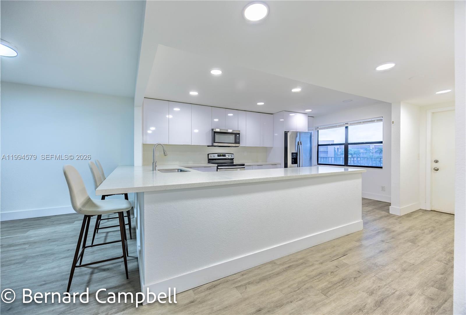 A modern kitchen features white cabinetry, stainless steel appliances, and a large breakfast bar island — 2606 NW 104th Ave # 303, Sunrise FL 33322, SUNRISE, FL