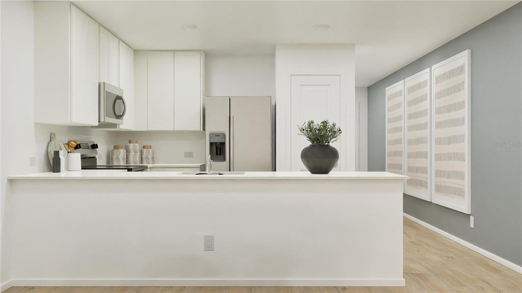 A modern kitchen features white cabinetry, stainless steel appliances, and a white breakfast bar — 5609 MORANT BAY PATH, KISSIMMEE, FL