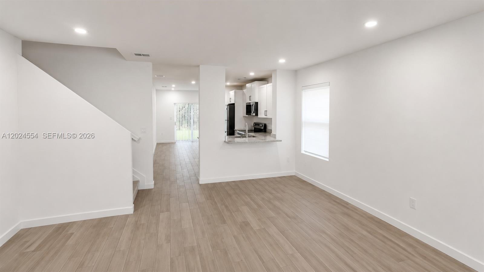 An open-concept living area features light wood-look flooring, white walls, and a kitchen pass-through — 619 NE 4th St, Florida City FL 33034, FLORIDA CITY, FL