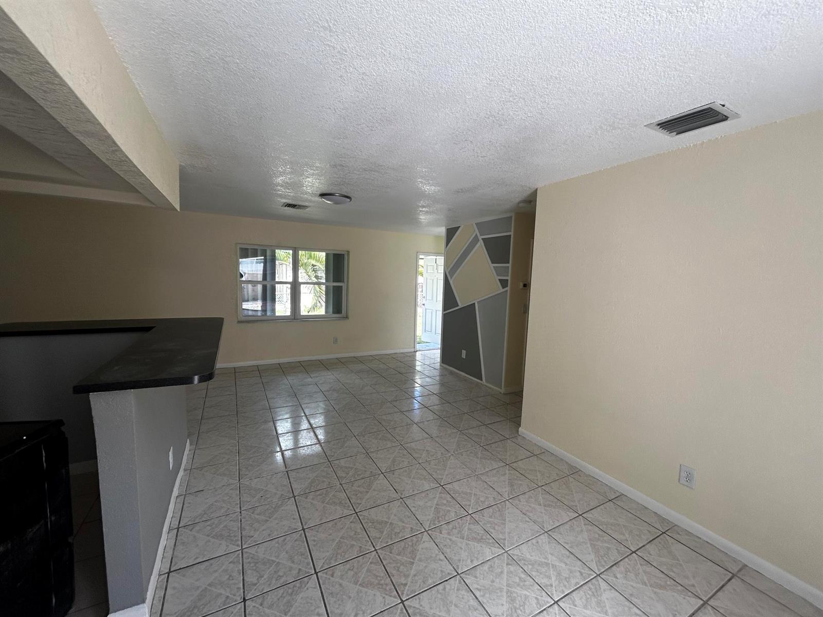 An open-concept living area features light-colored tile flooring, beige walls, and a geometric accent wall — 2691 NW 8th Street, Pompano Beach FL 33069, POMPANO BEACH, FL