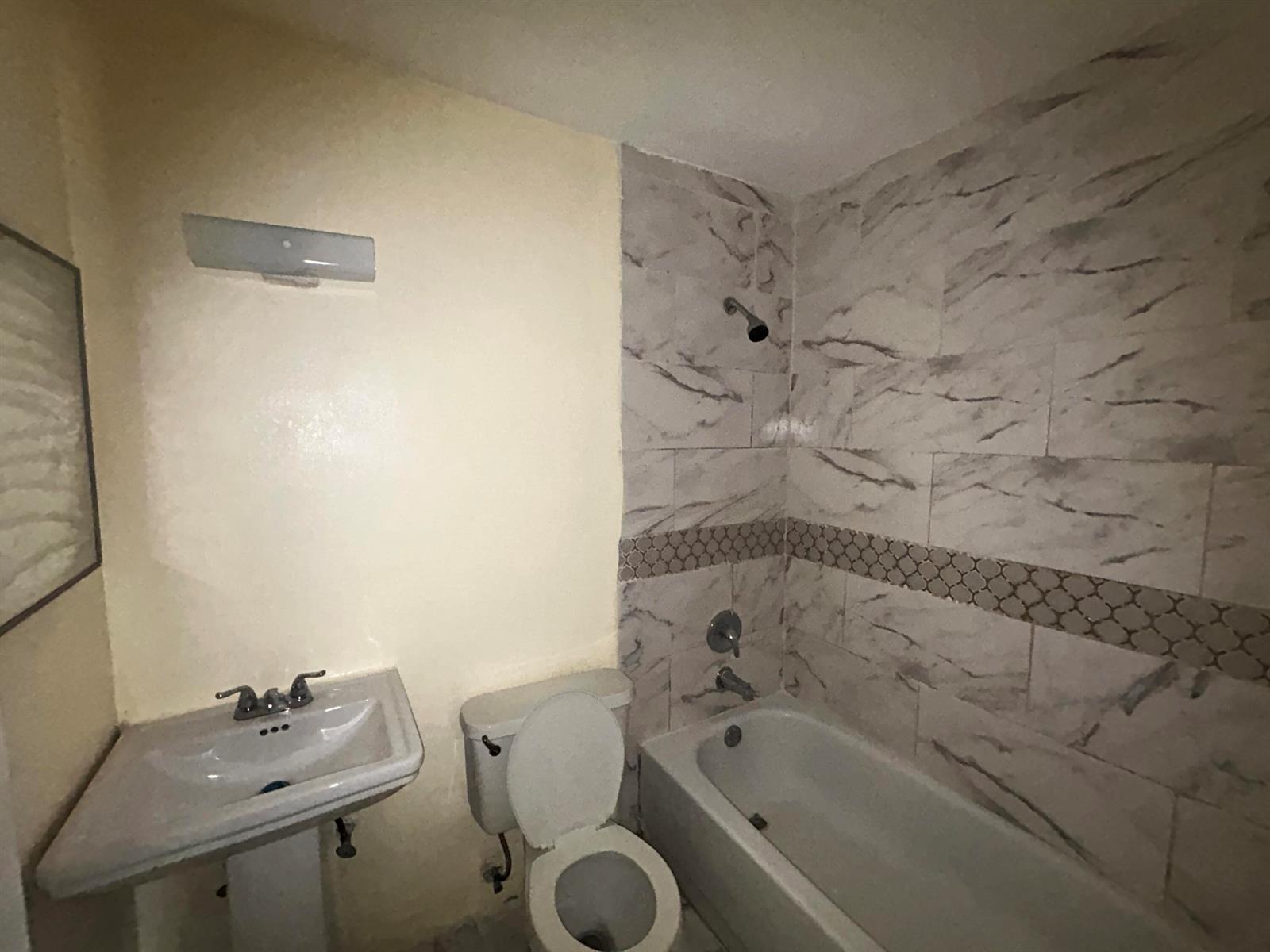 A bathroom features a pedestal sink, a toilet, and a bathtub with marble-patterned tile walls — 2691 NW 8th Street, Pompano Beach FL 33069, POMPANO BEACH, FL