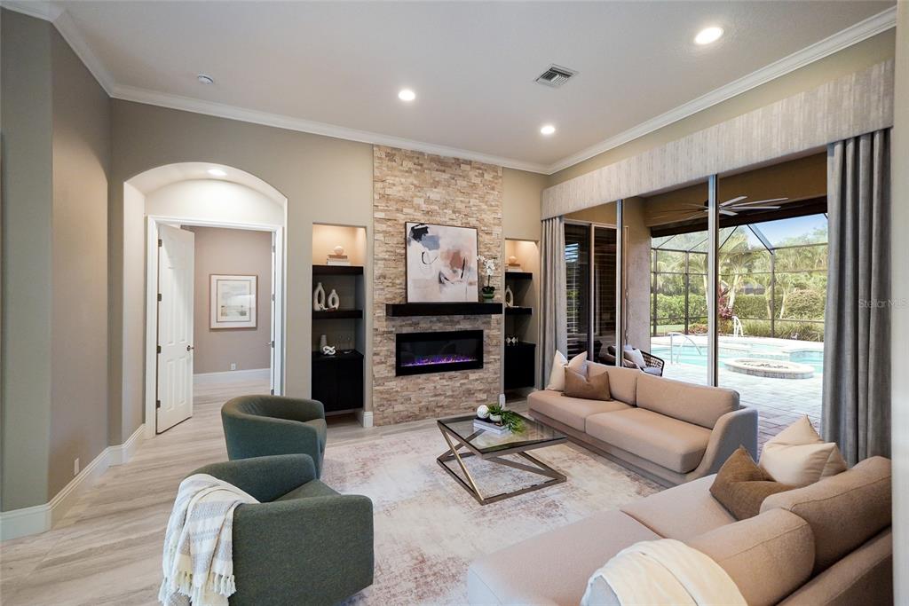 A living room features a stone fireplace, built-in shelves, and sliding doors opening to a pool — 8122 LONE TREE GLEN, LAKEWOOD RANCH, FL