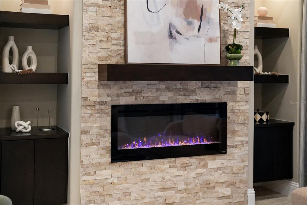 A stone-clad fireplace with a dark wood mantel sits between built-in shelves and cabinets — 8122 LONE TREE GLEN, LAKEWOOD RANCH, FL