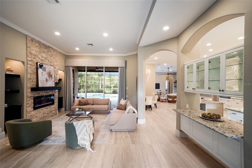 A living room with a stone fireplace, light wood floors, and an adjacent kitchen area — 8122 LONE TREE GLEN, LAKEWOOD RANCH, FL