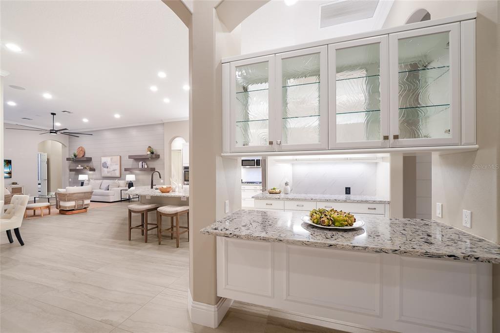 A kitchen features white cabinetry, granite countertops, and a view into an adjacent living area — 8122 LONE TREE GLEN, LAKEWOOD RANCH, FL
