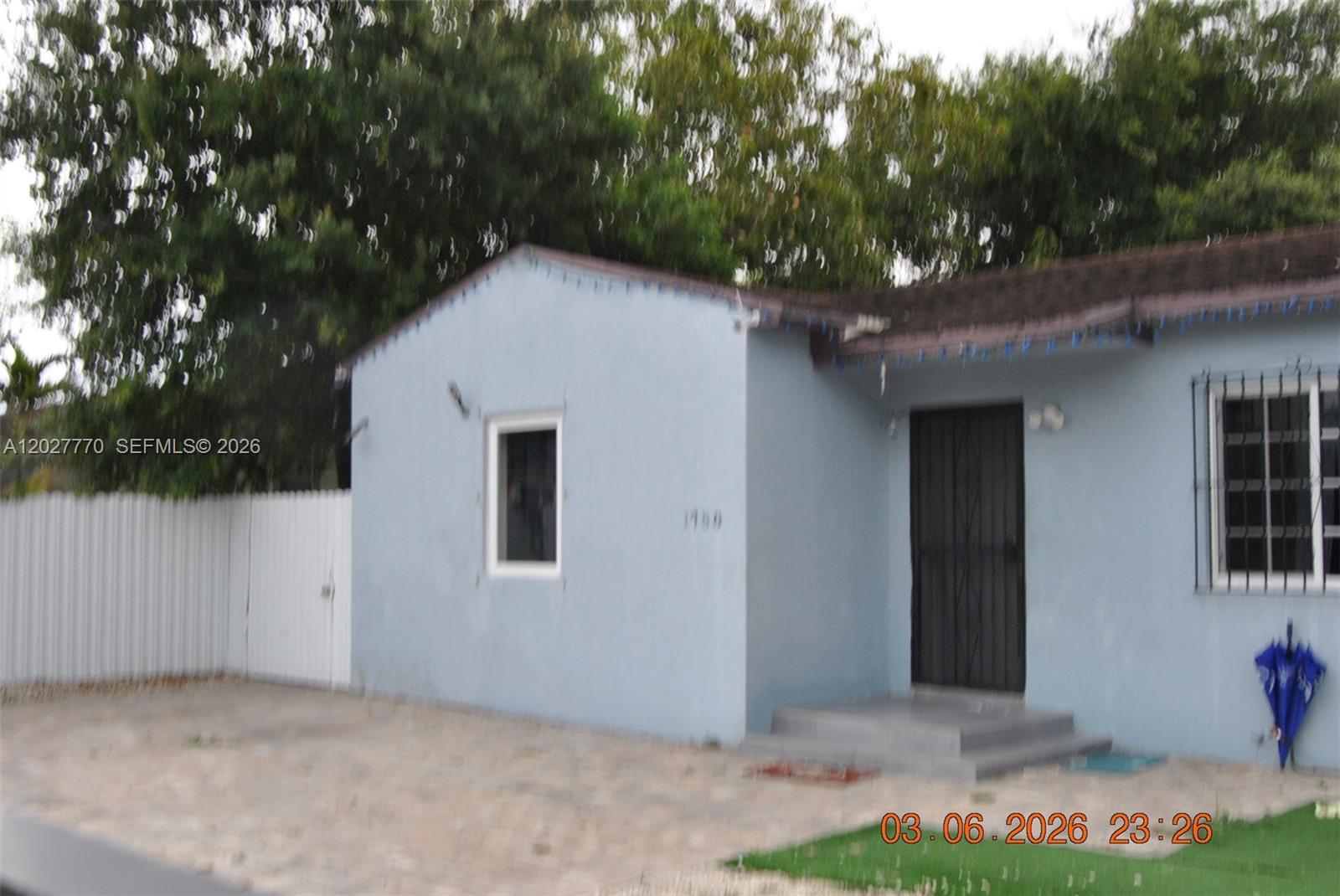 A light blue single-story house features a front door, two windows, and a white fence — 1750 NW 55th Ter, Miami FL 33142, MIAMI, FL