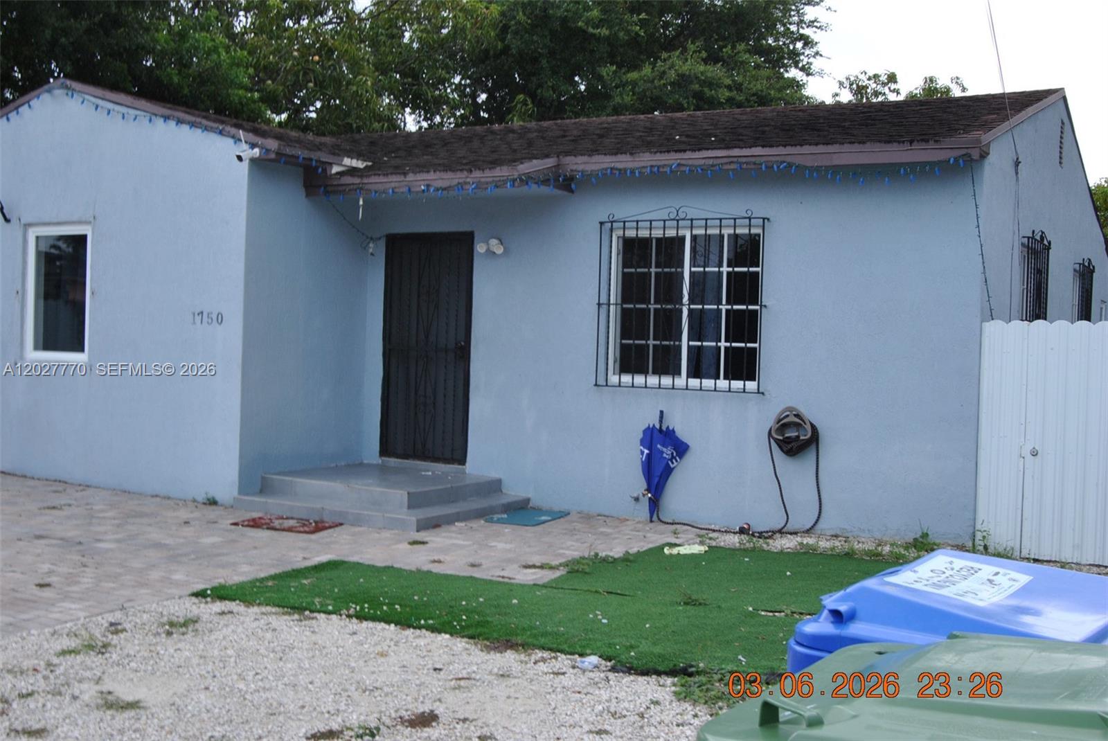 A light blue single-story house features a front door, a window with security bars, and a gravel yard — 1750 NW 55th Ter, Miami FL 33142, MIAMI, FL