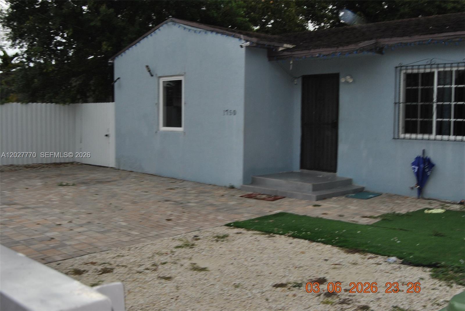 A light blue house features a paved driveway, a small front porch, and a white fence — 1750 NW 55th Ter, Miami FL 33142, MIAMI, FL