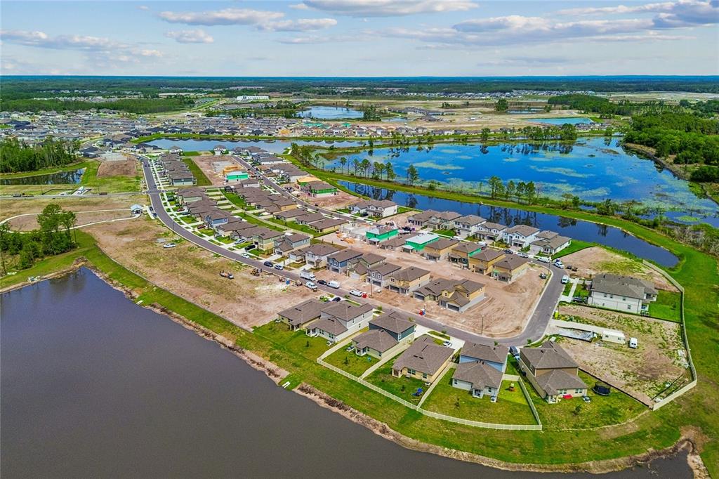 An aerial view shows a suburban neighborhood with new houses under construction near a lake — 7671 PAINTED SKY PLACE, LAND O LAKES, FL