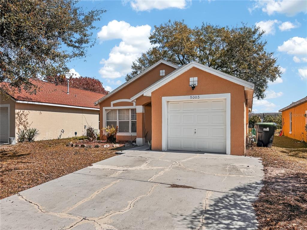 A single-story orange stucco house with a white garage door and a cracked concrete driveway — 5003 AVENTURA BOULEVARD, ORLANDO, FL
