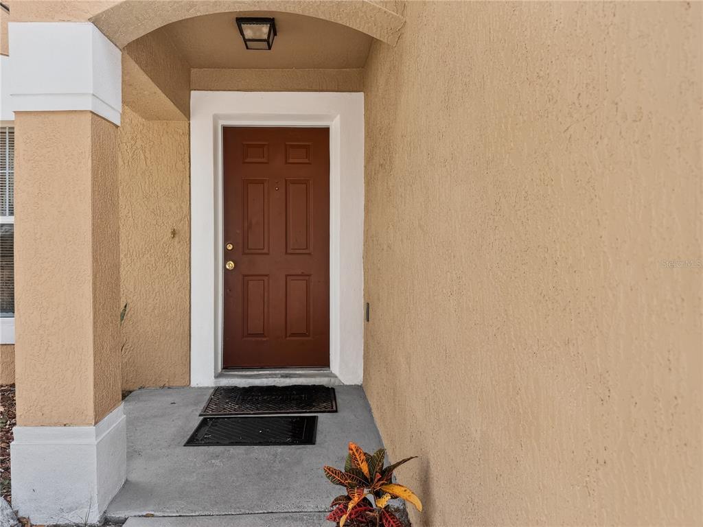 A brown front door is set within a tan stucco entryway with a concrete porch — 5003 AVENTURA BOULEVARD, ORLANDO, FL