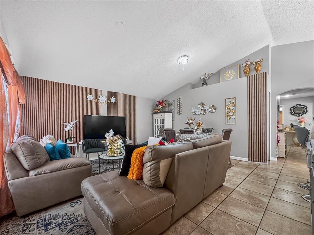 A living room features a brown sectional sofa, wood-slat accent walls, and tile flooring — 5003 AVENTURA BOULEVARD, ORLANDO, FL