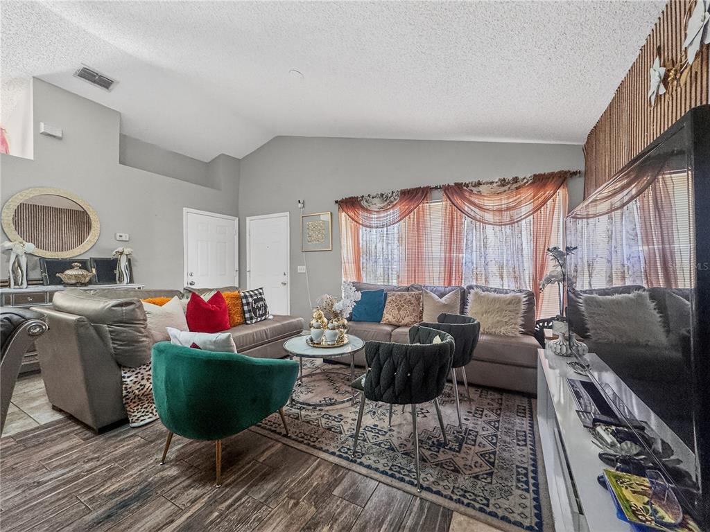A living room features a sectional sofa, accent chairs, a patterned rug, and vaulted ceilings — 5003 AVENTURA BOULEVARD, ORLANDO, FL