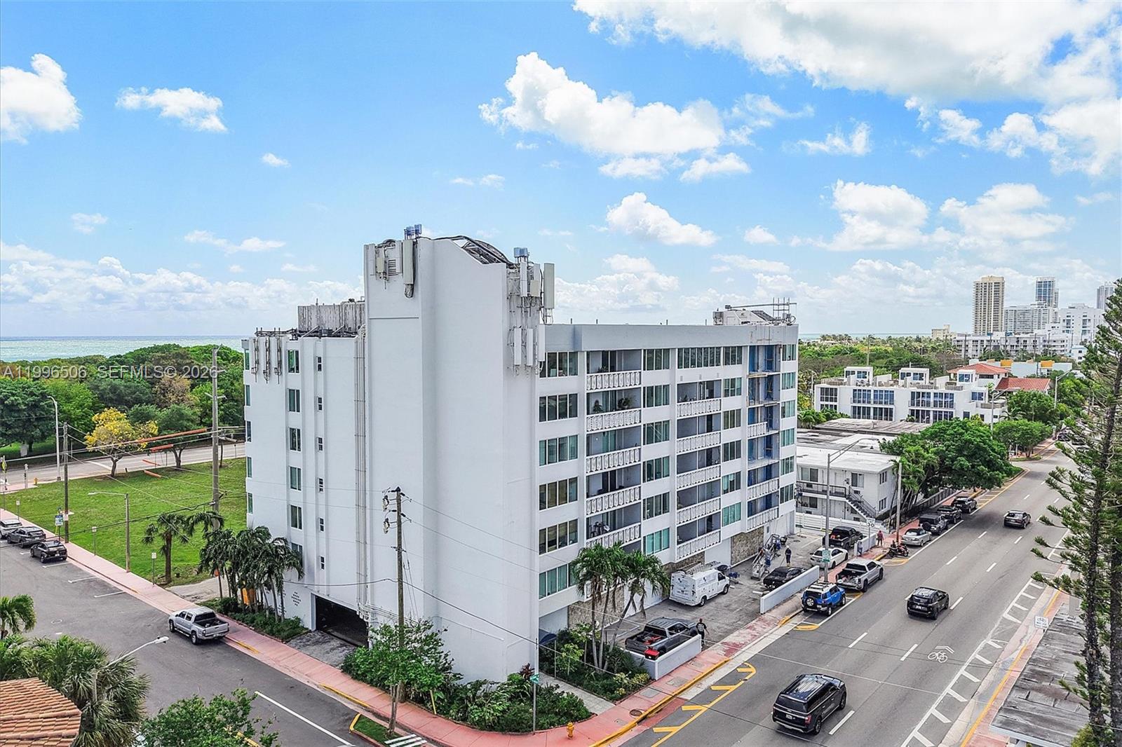 An exterior view of a multi-story white apartment building situated near a road and trees — 8233 Harding Ave # 504, Miami Beach FL 33141, MIAMI BEACH, FL