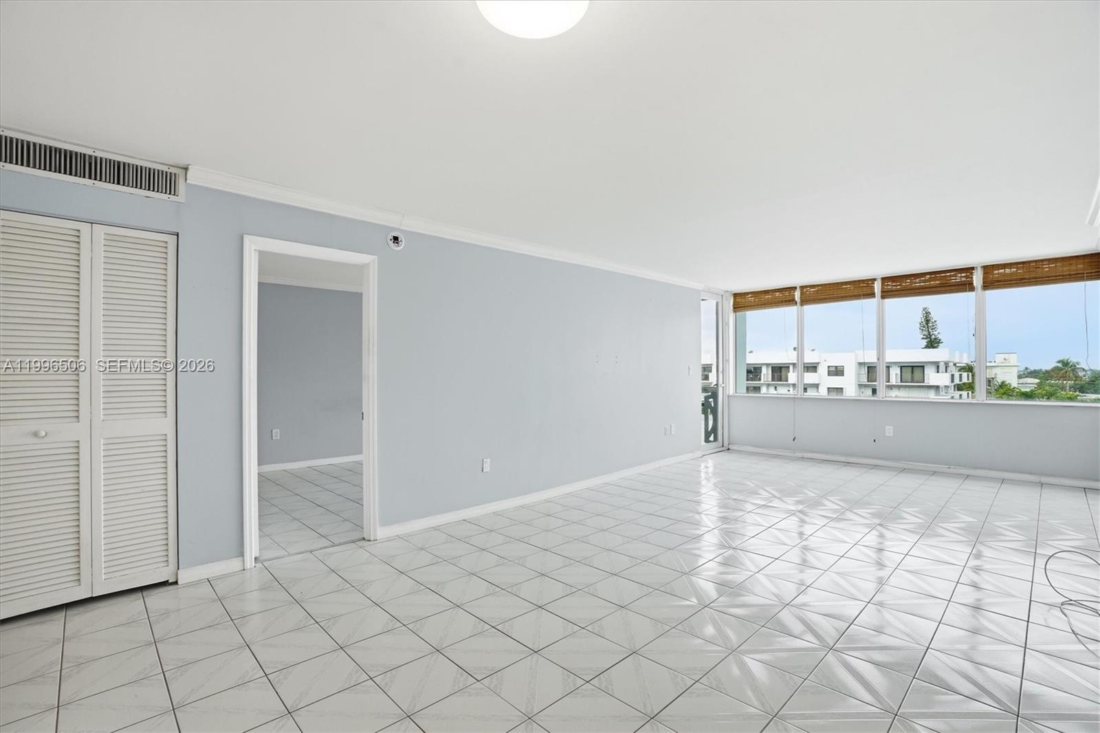 An empty room features light-colored tile flooring, pale blue walls, and large windows with blinds — 8233 Harding Ave # 504, Miami Beach FL 33141, MIAMI BEACH, FL